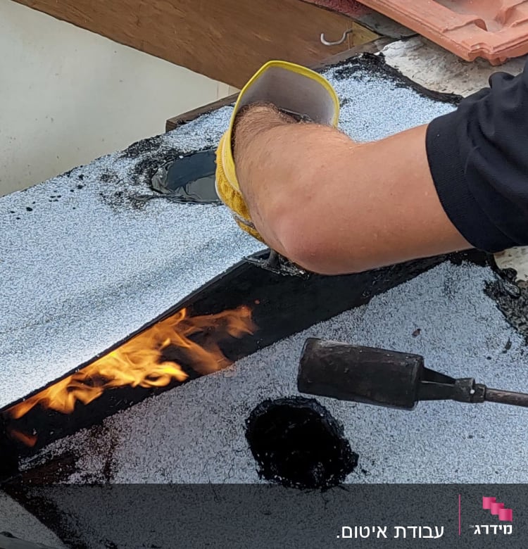 אדם משתמש במבער לאיטום גג עם יריעות ביטומניות